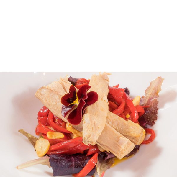 Filetes de melva canutera con pimientos rojos, ajo, hojas verdes y una flor comestible